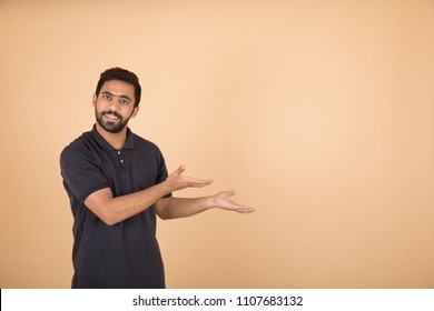 Handsome Young Man Wearing A Casual Outfit, Doing Welcome Sign, On His Face Big Smile, Standing On An Orange Background.