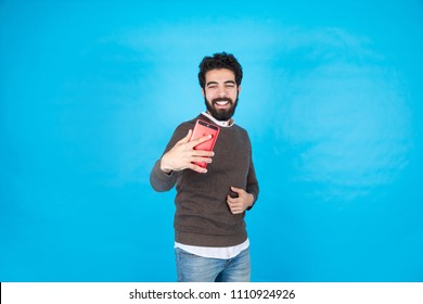 Handsome young man wearing a casual outfit taking a selfie by his phone and smiling, standing on a blue background. - Powered by Shutterstock