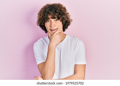 Handsome young man wearing casual white t shirt looking confident at the camera smiling with crossed arms and hand raised on chin. thinking positive. 