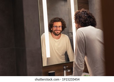 Handsome Young Man Wearing Pajamas Standing In Front Of Mirror In Bathroom, Getting Ready For Bed, Brushing Teeth And Washing His Face