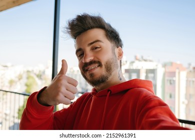 Handsome young man wearing red hoodie taking a self portrait outdoor at balcony. Happy guy smiling on camera with thumb up while taking selfie. - Powered by Shutterstock