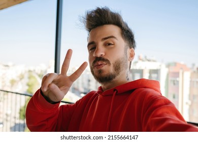 Handsome young man wearing red hoodie taking a self portrait outdoor at balcony. Happy guy smiling at the camera. Photo of handsome happy young man make selfie by camera. Showing v-sign. - Powered by Shutterstock