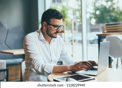 Handsome young man wearing white shirt and eye glasses sitting with laptop and working in cafe, freelance concept,close up portrait. - Shutterstock ID 1128229949