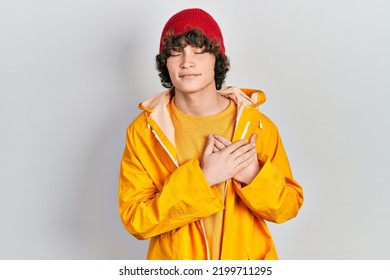 Handsome young man wearing yellow raincoat smiling with hands on chest with closed eyes and grateful gesture on face. health concept.  - Shutterstock ID 2199711295