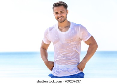 Handsome young man in wet t-shirt on sea beach