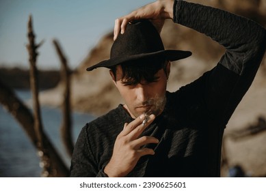 Handsome young man in a wide-brimmed hat smokes on the beach - Powered by Shutterstock