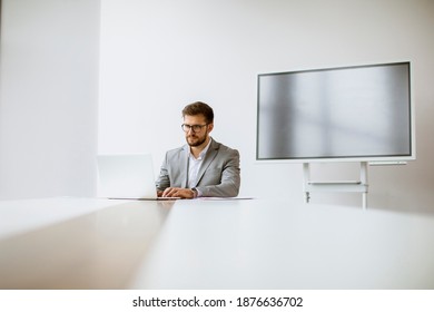 Handsome Young Man Working On Laptop In Bright Office With Big Screen Behind Him