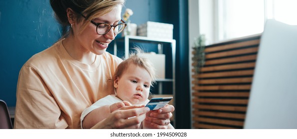 Handsome young mother with cute little baby using bank credit card and doing online shopping and payment from home - Shutterstock ID 1994509028