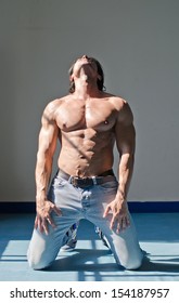 Handsome Young Muscle Man Shirtless Kneeling On The Floor, Holding Head Up, Wearing Jeans