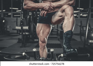 Handsome young muscular Caucasian man of model appearance working out in the gym training legs quadriceps and hamstrings on machines and with a barbell pumping up fitness and bodybuilding concept
