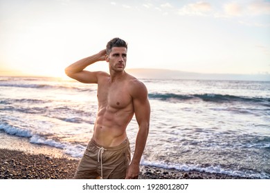 Handsome young muscular italian man posing shirtless on the beach, sunset summer time. Ideal fit body. 