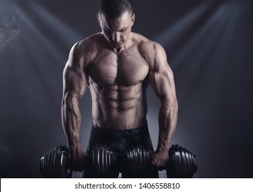 Handsome young muscular man exercising with dumbbell on dark background - Shutterstock ID 1406558810