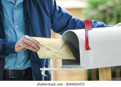 Handsome young postman putting letter in mail box outdoors