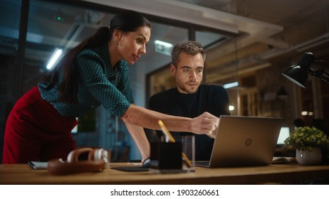 Handsome Young Project Manager And Beautiful Creative Director Work And Talk About Business Strategy On A Laptop Computer In Creative Office. Life Of A Busy Marketing Agency In Modern Loft Building.