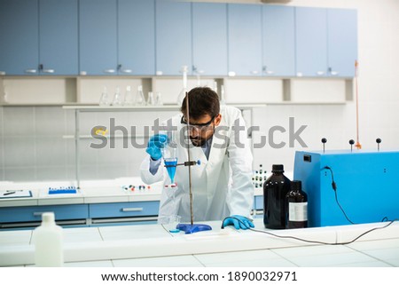 Handsome young researcher working with blue liquid at separatory funnel in the laboratory