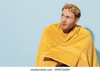 Handsome Young Sad Man In Red Shorts Swimsuit Warepped In Yellow Towel Relax Near Hotel Pool In Cold Cloudy Weather Look Aside Isolated On Pastel Blue Background Summer Vacation Sea Sun Tan Concept