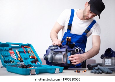 Handsome Young Serviceman Is Repairing Modern Vacuum Cleaner In His Office