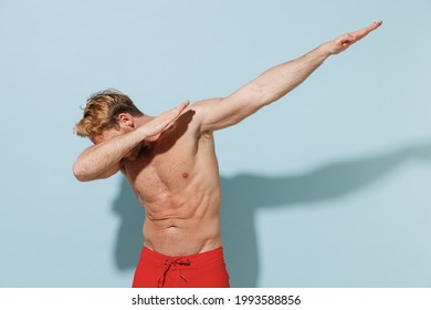 Handsome Young Sexy Man In Red Shorts Swimsuit Relax Near Hotel Pool Do Dab Hip Hop Dance Hand Move Gesture Youth Sign Cover Face Isolated On Blue Background. Summer Vacation Sea Rest Sun Tan Concept