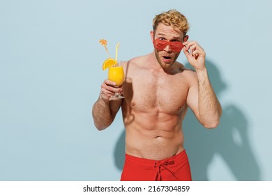 Handsome Young Sexy Sporty Man In Red Shorts Swimsuit Took Off Glasses Relax Near Hotel Pool Hold Orange Alcohol Cocktail Isolated On Pastel Blue Background Summer Vacation Sea Rest Sun Tan Concept