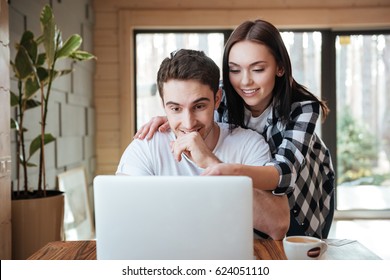 Handsome young sitting man and his pretty woman surfing the internet using laptop in living room