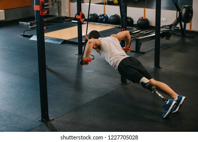 handsome young sportsman with artificial leg doing push ups with hanging rings of gymnastics ladder at gym - Powered by Shutterstock