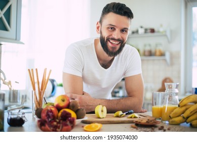 Handsome young sporty smiling man in the kitchen is preparing vegan healthy fruits salad and smoothie in a good mood - Powered by Shutterstock