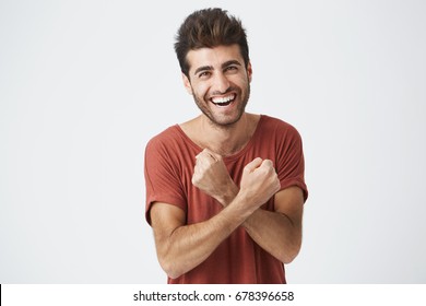 Handsome young sun-tanned man feeling excited, gesturing actively, keeping fists clenched and crossed, joyfully laughing, happy with good luck. Student excited by successful passing of exams.