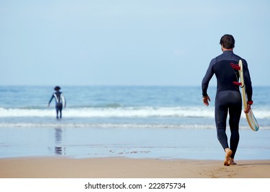 Handsome young surfer man walking at ocean beach holding his surfing board, muscular build surfer carrying surfboard while walking on the beach, men ready to surfing walk on the sand holding board