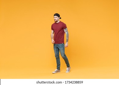 Handsome young tattooed man guy in casual t-shirt black cap posing isolated on yellow wall background studio portrait. People sincere emotions lifestyle concept. Mock up copy space. Looking aside