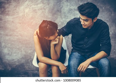 Handsome Young Teen Asian Teen Girls Entwined Hands, Shoulders, Show Love And Smile At Each Other Happily. He Had Two People Sitting On A Chair With White Cement Wall As A Background.