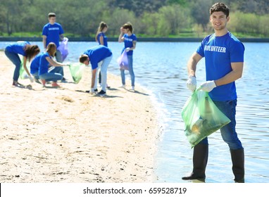 Handsome young volunteer with team gathering garbage on river bank - Powered by Shutterstock