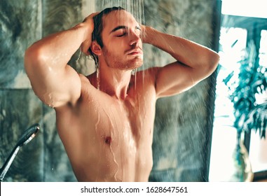 Handsoome muscular man taking shower in light modern bathroom.