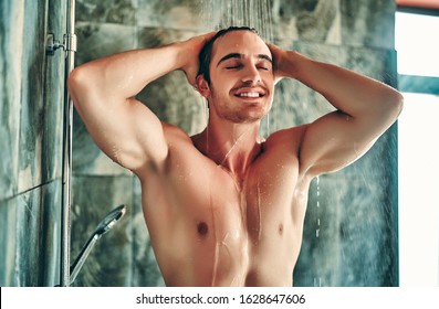 Handsoome muscular man taking shower in light modern bathroom.