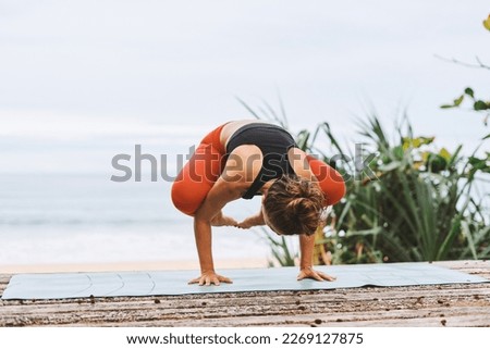 Handstand balancing Young athletic woman in black sport bra, red pants doing yoga exercises in front of seashore, sea, beach in nature. Health care, mental health, wellbeing through meditation, sport