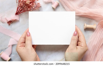 Handswith A Blank Card Over A Marble Near Dried Pink Flowers And Silk Ribbons Top View. Flat Lay With Horizontal Blank Card. Romantic Thank You Or Rsvp Card Mockup, Copy Space