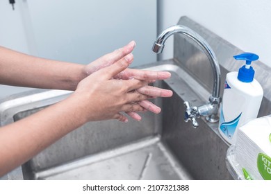 Handwashing Technique - Rubbing Hands Together With Interlaced Fingers. Using Liquid Soap And At A Stainless Sink. At A Clinic Or Laboratory.