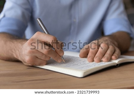 Handwriting. Cropped close up view of male student hands hold pencil write take notes of lecture course to paper copybook on desk. Young businessman record financial information plan workload for day