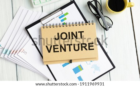 Handwriting text writing Joint Venture. Concept meaning Collaboration Arrangement Parties Partnership Team marker notebook paper communicating ideas Wooden background.