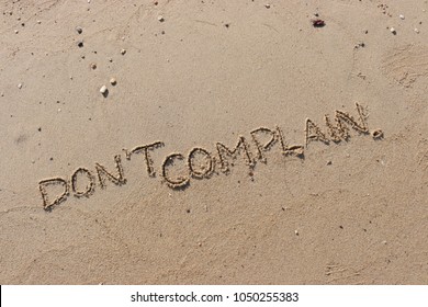 Handwriting  words "DON'T COMPLAIN." on sand of beach.