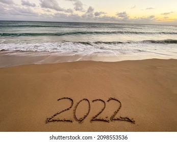 Handwriting year 2022 on sand on beach with waves and sky

