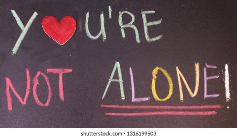 handwriting you are not alone on chalkboard with colorful chalk and wooden heart