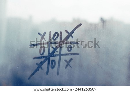 Handwritten doodle tic-tac-toe game with winning game crossed out on misted blue glass sunset window with raindrops, concept