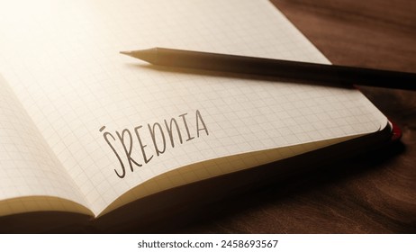 A handwritten inscription "Średnia" on a grille of an open notebook on a wooden countertop, next to a black pencil, lighting of light. (selective focus), translation: mean