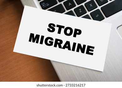 Handwritten note displaying the words STOP MIGRAINE on a white paper placed on a laptop keyboard. This image symbolizes health awareness and pain management strategies.