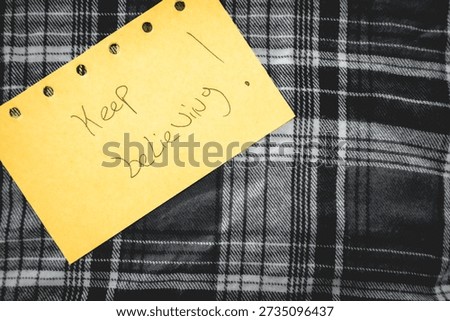 A handwritten note with Keep believing on it. Positive notes. on a textile  background.