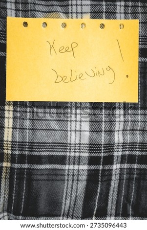 A handwritten note with Keep believing on it. Positive notes. on a textile  background.