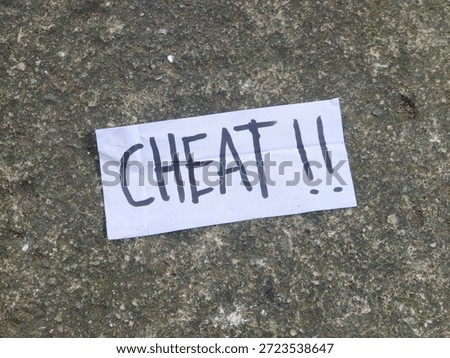 Handwritten Note on Rough Surface, Expressing Deception, Warning of Dishonesty in Relationships, The Word "CHEAT !!" on White Paper, Found on an Urban Sidewalk, or Public Grounds, rectangular piece of white paper with the word "CHEAT !!" written in bold, black, hand-drawn letters, accompanied by two exclamation marks. The note is placed on a rough, dark, and textured ground surface that appears to be concrete or asphalt, highlighting the strong, emotional message against a dull, photo object, design material, graphic resource, raw picture, editable image, cut out, removable background 