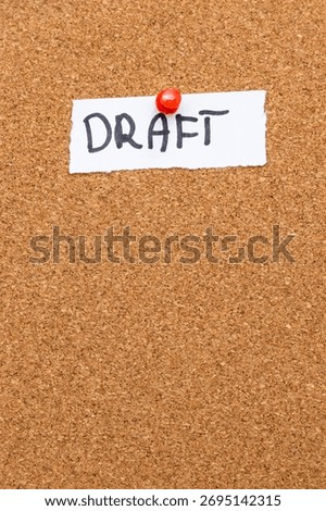 A handwritten note stating DRAFT pinned on a corkboard. The rustic texture of cork complements the messages significance in creative processes and revisions.