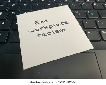 A handwritten note stating end workplace racism on a computer keyboard
