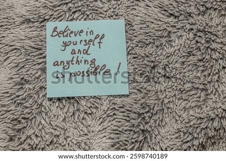 A handwritten note with an uplifting message rests on a cozy, textured surface. The message promotes self-belief and the endless possibilities that follow.